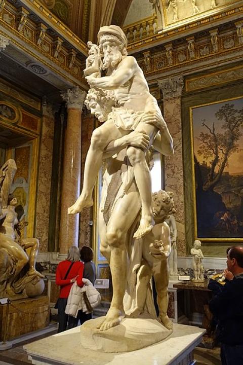 A white marble statue of a nude man holding a smaller old man on his shoulder with a child behind his legs. The old man carries a statue.