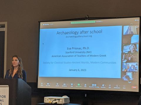 A long-haired woman stands at a podium with a Zoom screen behind her. A Powerpoint on the Zoom screen reads "Archaeology After School."