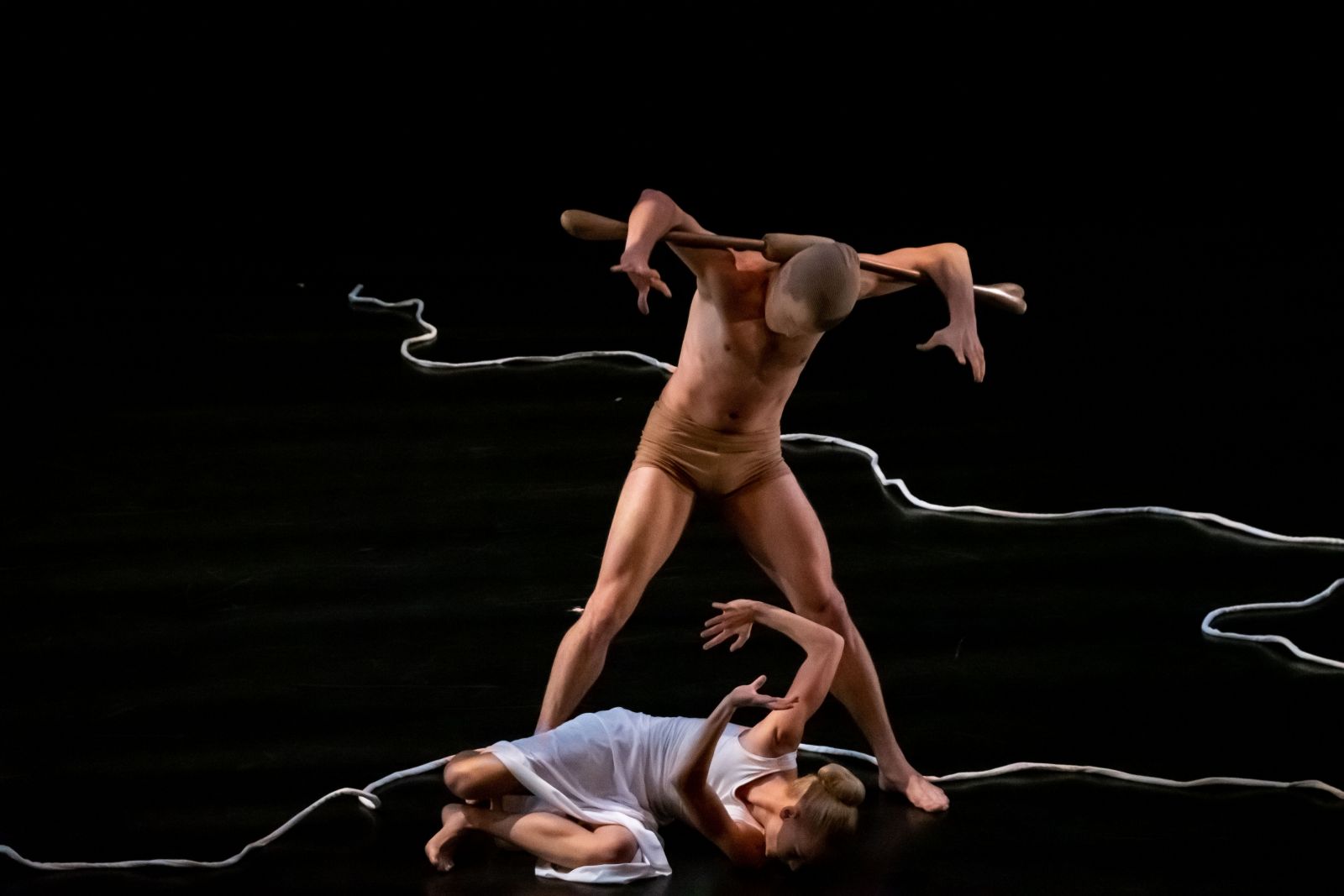 A mostly-nude man stands over a woman, menacing her and wearing faux bull horns. She lies on the ground with her arms up in protection.