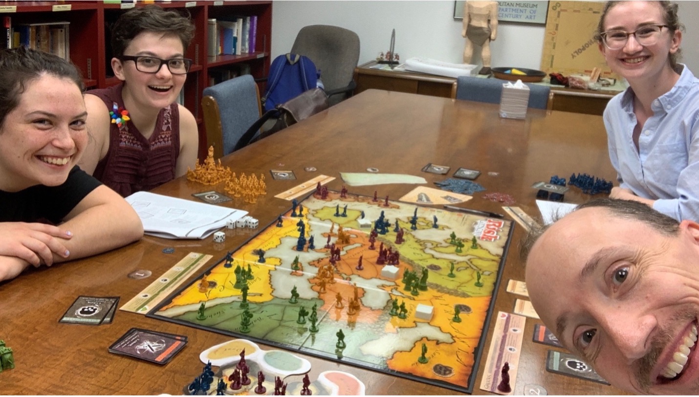 Four people sit around a table that has a board game set up on it. 