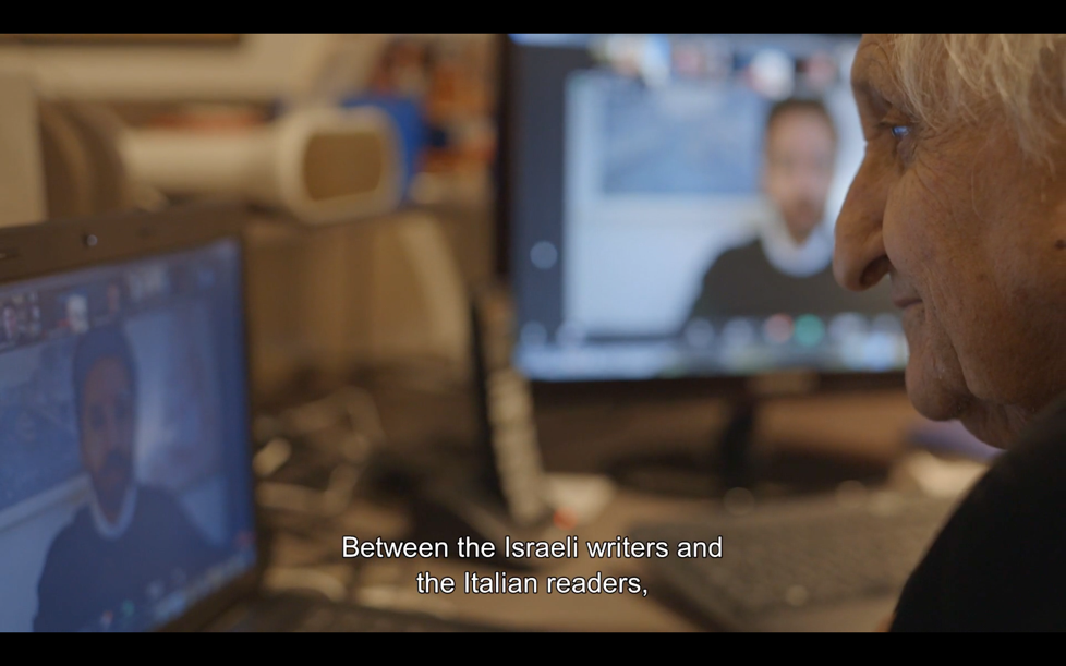The same man looks at a computer screen, where a video call is taking place. The caption reads "Between the Israeli writers and the Italian readers"